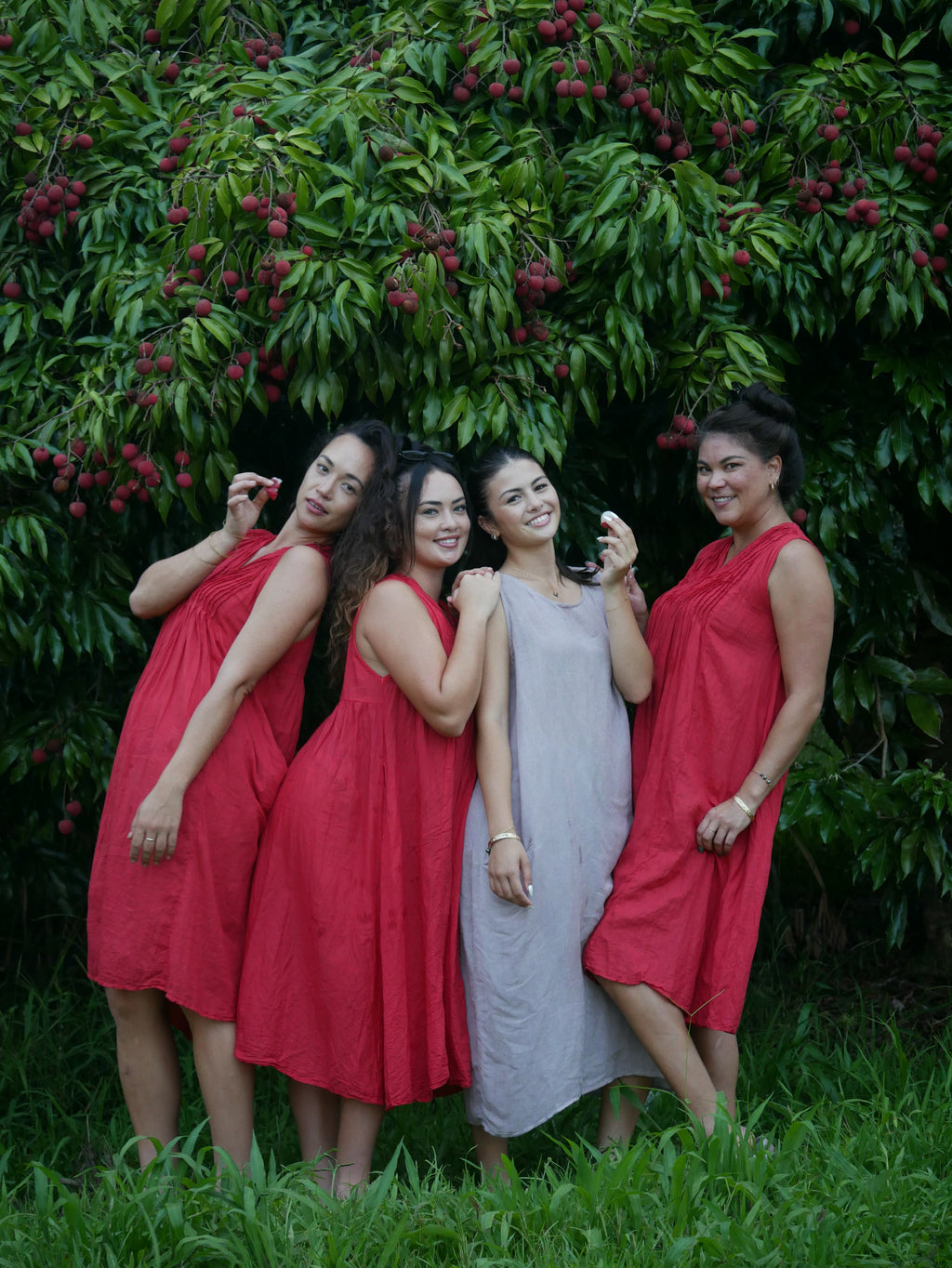 Model in a deep lychee-red cotton A-line dress with V-neckline and pockets, photographed on a Hilo farm.