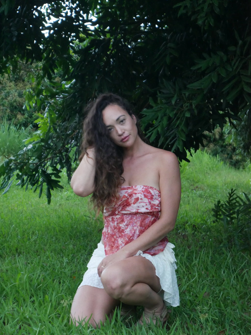 Model in a warm red shibori tie-dye silk wrap scarf, photographed at Olson Keolanui Farms in Hilo.